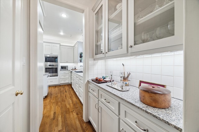 kitchen featuring light stone counters, white cabinetry, appliances with stainless steel finishes, backsplash, and glass insert cabinets