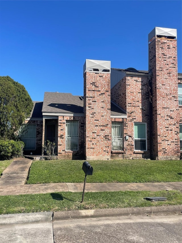 view of front of house featuring brick siding, a shingled roof, a chimney, and a front yard