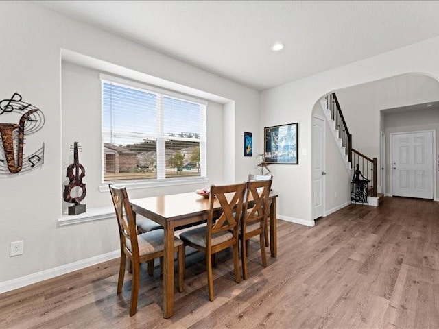 dining room featuring arched walkways, wood finished floors, stairs, and baseboards