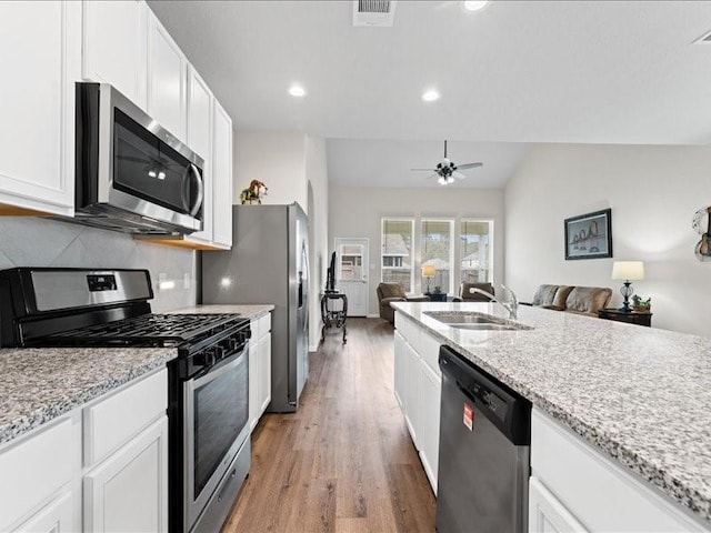 kitchen with open floor plan, a sink, stainless steel appliances, white cabinetry, and backsplash