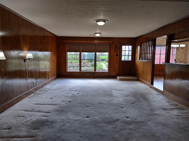 unfurnished living room with carpet floors, a textured ceiling, and wood walls