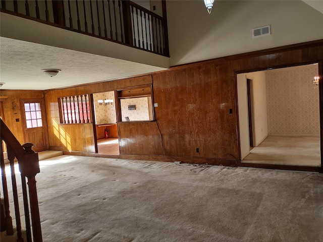 interior space with stairway, carpet, visible vents, wood walls, and a textured ceiling