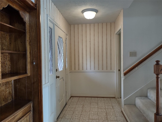 doorway to outside featuring stairway, light floors, wallpapered walls, and a textured ceiling