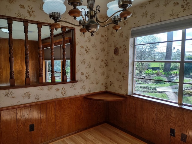 unfurnished dining area featuring wallpapered walls, an inviting chandelier, light wood-style floors, and wainscoting