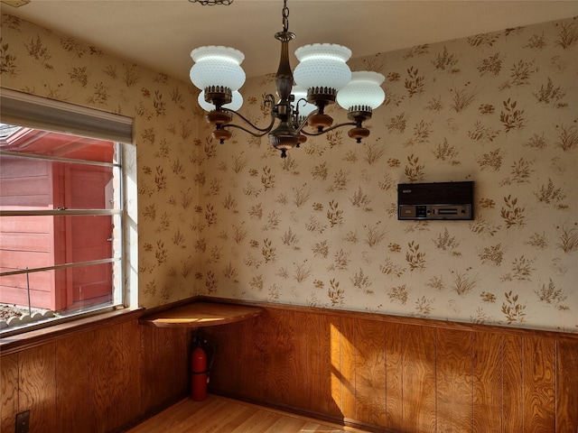 unfurnished dining area with a chandelier, a wainscoted wall, wallpapered walls, and light wood-style floors