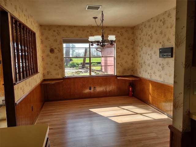 unfurnished dining area with wallpapered walls, an inviting chandelier, wood finished floors, and a wainscoted wall