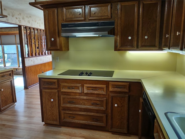 kitchen featuring light wood-style flooring, a sink, black appliances, light countertops, and under cabinet range hood