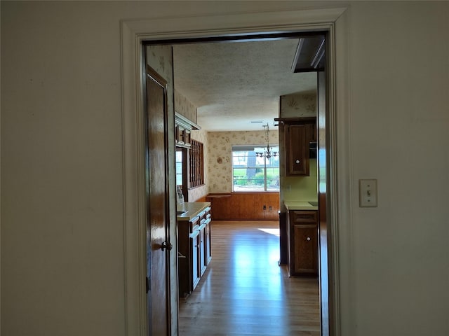 corridor with wallpapered walls, a notable chandelier, light wood-type flooring, and a textured ceiling