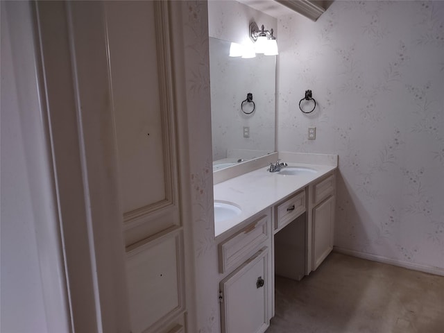 bathroom featuring a sink, wallpapered walls, baseboards, and double vanity