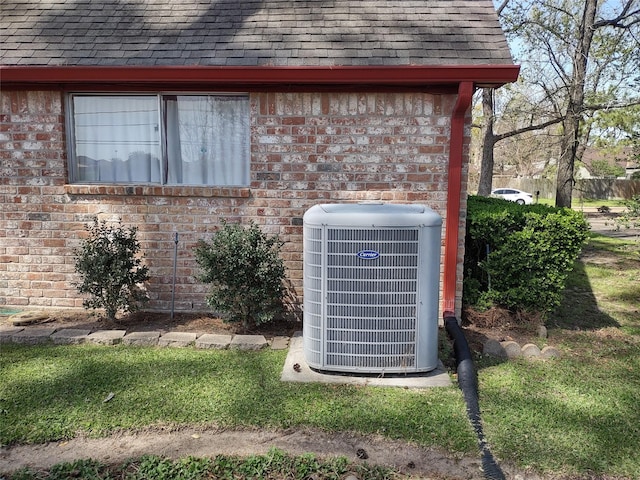 exterior details featuring a downspout, cooling unit, gutters, a shingled roof, and brick siding