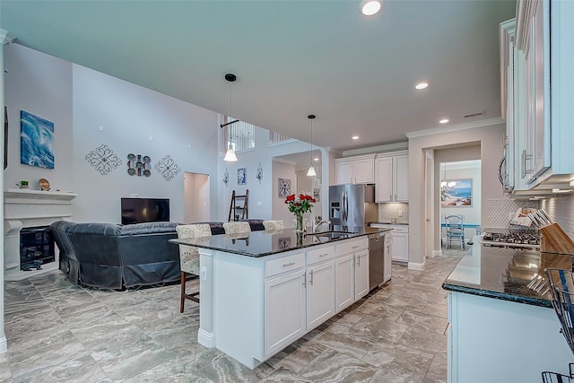 kitchen featuring tasteful backsplash, white cabinets, an island with sink, appliances with stainless steel finishes, and pendant lighting