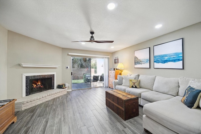 living room with recessed lighting, a brick fireplace, a textured ceiling, and wood finished floors