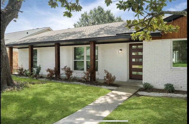 entrance to property featuring roof with shingles, a lawn, and brick siding