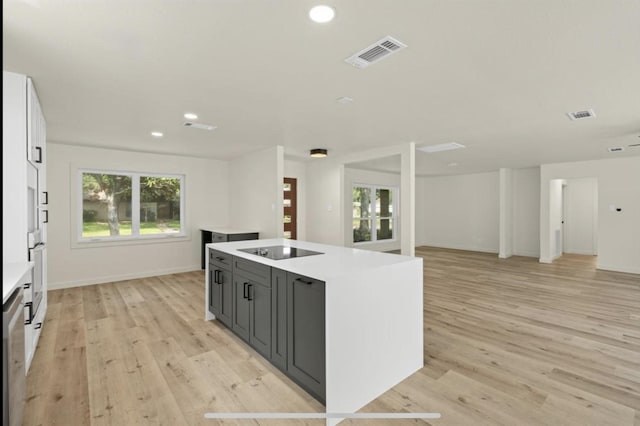 kitchen with light countertops, visible vents, open floor plan, a kitchen island with sink, and black electric cooktop