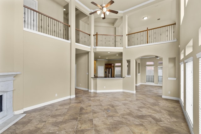 unfurnished living room with ceiling fan, baseboards, a fireplace with raised hearth, and arched walkways