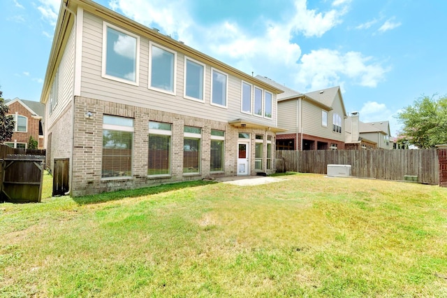 rear view of house featuring brick siding, a lawn, and a fenced backyard