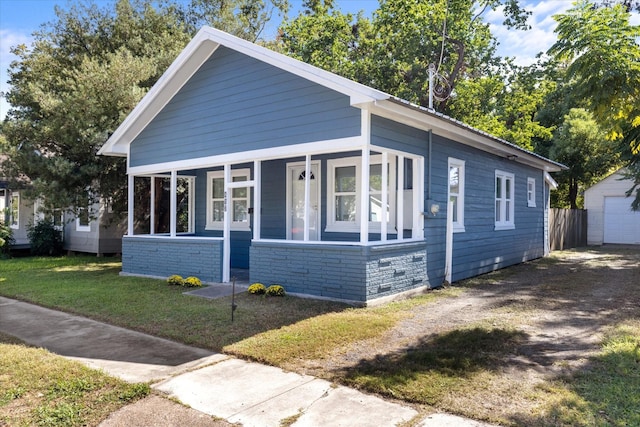 bungalow-style house featuring dirt driveway, a porch, a garage, stone siding, and a front lawn