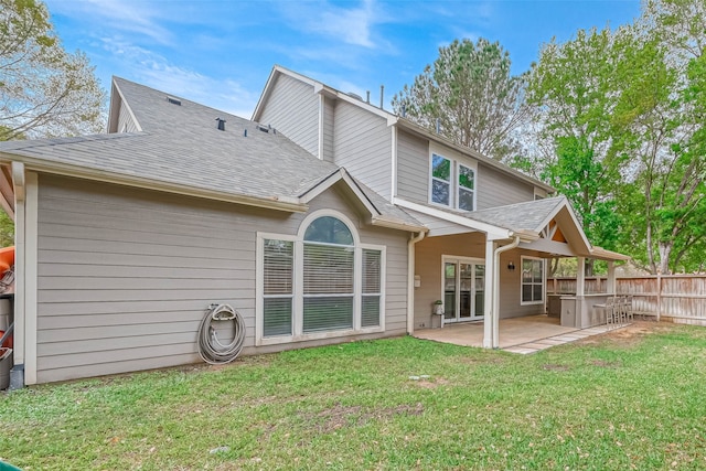 rear view of property featuring a patio, fence, a yard, roof with shingles, and a hot tub