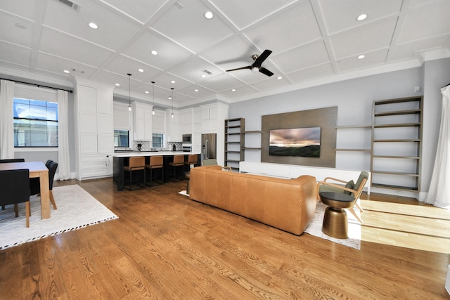 living room featuring light wood finished floors, crown molding, coffered ceiling, and a ceiling fan