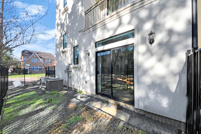 view of exterior entry with cooling unit, fence, and stucco siding