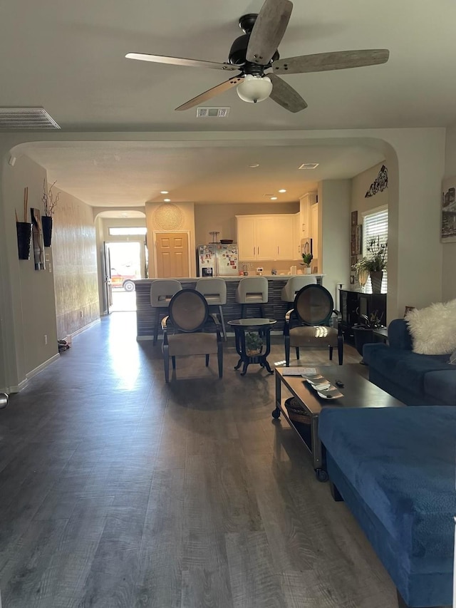 living area featuring arched walkways, dark wood-style flooring, plenty of natural light, and visible vents