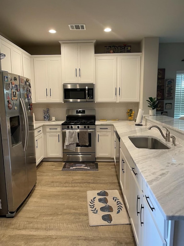 kitchen featuring a peninsula, light stone countertops, stainless steel appliances, white cabinetry, and a sink