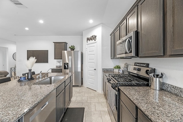 kitchen featuring visible vents, light stone countertops, stainless steel appliances, dark brown cabinets, and a sink