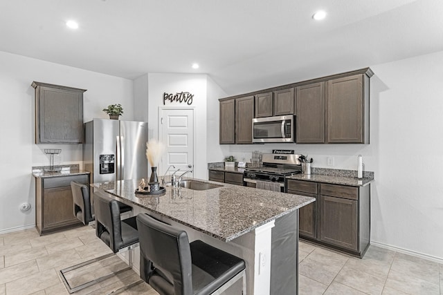 kitchen featuring a center island with sink, appliances with stainless steel finishes, a breakfast bar area, stone counters, and a sink