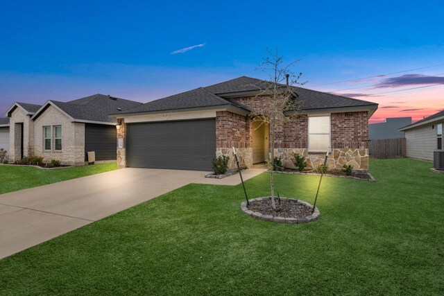 ranch-style home featuring a garage, driveway, a shingled roof, a yard, and brick siding