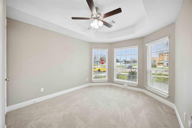 carpeted empty room with visible vents, baseboards, a raised ceiling, and a ceiling fan