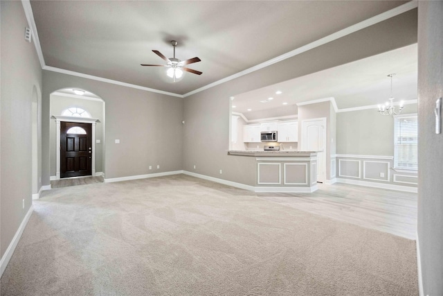 unfurnished living room featuring light carpet, ornamental molding, arched walkways, and ceiling fan with notable chandelier