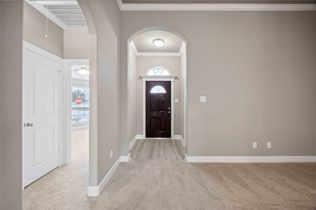 entryway with light carpet, ornamental molding, arched walkways, and baseboards