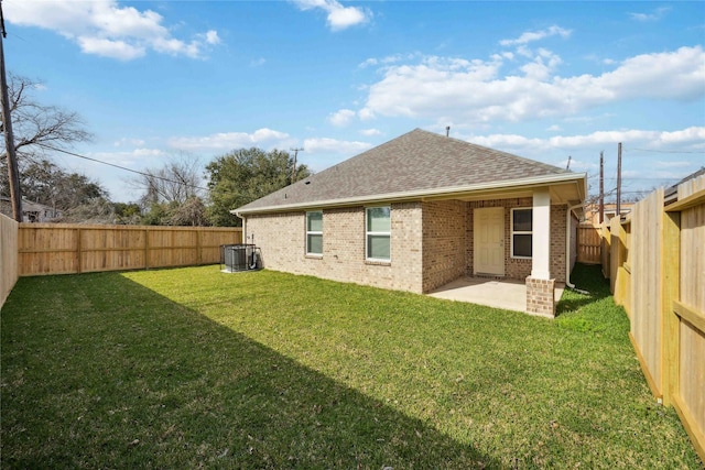 back of property featuring a shingled roof, cooling unit, a yard, a patio area, and brick siding