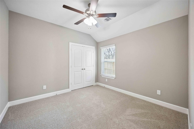 carpeted spare room with lofted ceiling, visible vents, baseboards, and a ceiling fan