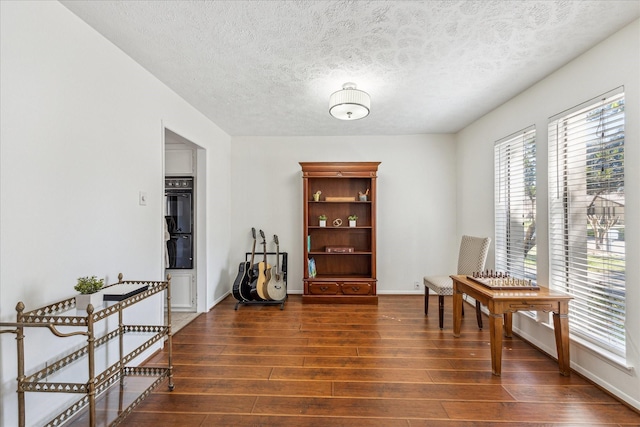 sitting room featuring dark wood-type flooring, a textured ceiling, and baseboards