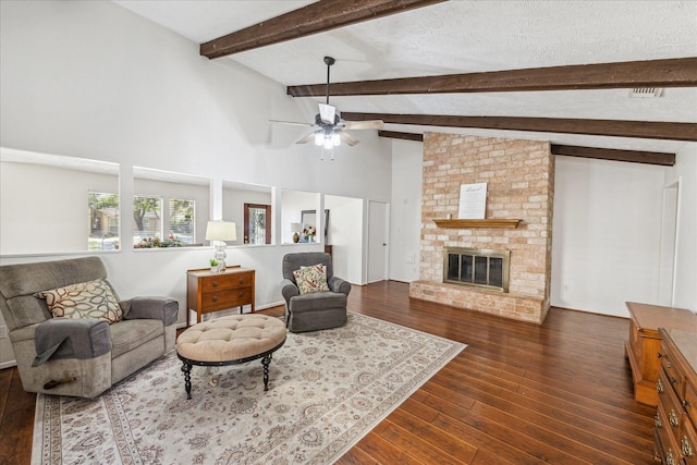 living area featuring dark wood finished floors, vaulted ceiling with beams, a fireplace, a ceiling fan, and a textured ceiling