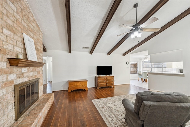 living area featuring vaulted ceiling with beams, a textured ceiling, hardwood / wood-style flooring, a fireplace, and visible vents