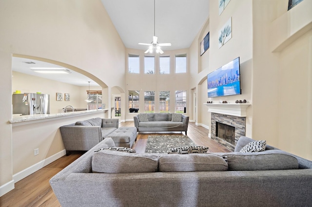 living area featuring arched walkways, ceiling fan, a fireplace, and wood finished floors