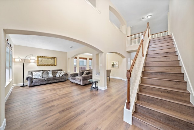 living area featuring stairs, light wood-type flooring, a towering ceiling, and baseboards