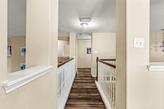 corridor with a textured ceiling, visible vents, dark wood-style flooring, and an upstairs landing