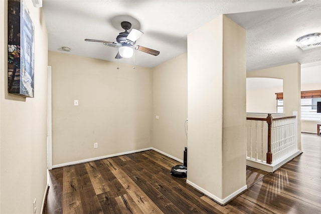 empty room with dark wood-style floors, arched walkways, ceiling fan, and baseboards