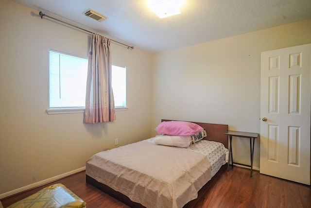 bedroom featuring visible vents, baseboards, a textured ceiling, and wood finished floors