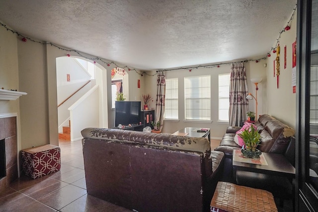 living area featuring tile patterned flooring, a tiled fireplace, stairway, and a textured ceiling