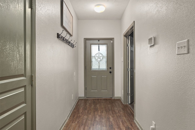 doorway to outside featuring a textured wall, dark wood-type flooring, and baseboards