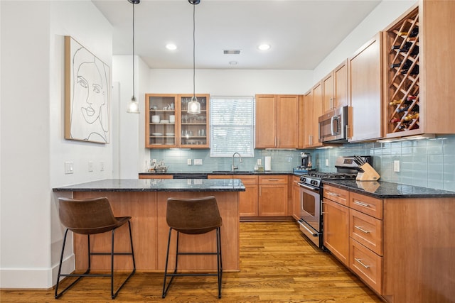 kitchen with glass insert cabinets, appliances with stainless steel finishes, hanging light fixtures, a kitchen bar, and a sink