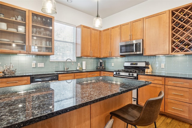 kitchen featuring a breakfast bar area, glass insert cabinets, stainless steel appliances, pendant lighting, and a sink