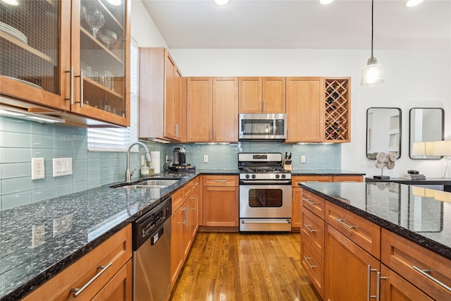 kitchen featuring dark stone counters, glass insert cabinets, appliances with stainless steel finishes, decorative light fixtures, and a sink