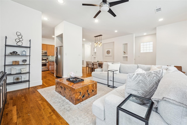 living area with ceiling fan with notable chandelier, recessed lighting, visible vents, and wood finished floors