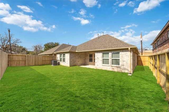 back of property with brick siding, a yard, a shingled roof, central AC unit, and a fenced backyard