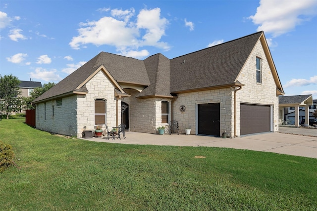 french provincial home featuring a shingled roof, an attached garage, a front yard, a patio area, and driveway